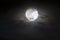 Big silver glowing Moon close-up on dark blue sky with scattered clouds.