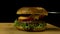 Big single cheeseburger isolated on black background. Stock footage. Close up of craft beef burger on wooden surface