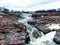 The Big Sioux River flows over rocks in Sioux Falls South Dakota with views of wildlife, ruins, park paths, train track bridge, tr