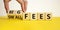 Big or small fees symbol. Businessman turns a wooden cube and changes words `small fees` to `big fees`. Beautiful yellow table