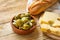 Big Spanish Green Gordal Olives with Herbs and Onions in Earthenware Bowl Baguette Maasdam Cheese on Cutting Board