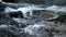 Big stone with small icicles in cold milky blurred water of mountain stream.