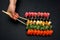 Big sushi set on a black plate background. A female hand holds two paar chopsticks. Top view