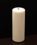 Big white candle isolated on black, standing on wooden table.