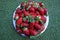 Big white plate with red strawberries on the grass background