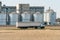 Big white truck on background large iron barrels of grain and granary elevator. Silver silos on agro manufacturing plant for