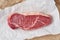 Big whole piece of raw beef meat, striploin on white parchment paper on craft background, zero waste packing