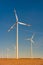 Big wind turbines to generate electrical power, green ecofriendly energy at blue sky standing in arid lifeless soil in warm sunset