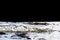 Big windy waves splashing over rocks. Wave splash in the lake on black background. Waves breaking on a stony beach, forming a spra