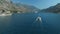 Big yacht and small sailing yacht sail along the Bay of Kotor, behind them there are beautiful mountains and cozy little