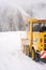 Big yellow snowplough with and helix is cleaning the road while a powerful stream of white snow go out