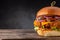 Big yummy chicken burger with cheese and pickles on a wooden board on a dark background.