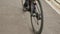 Bike wheel rotation. Woman cyclist is pedaling bike on promenade, close up of bike gear. Cyclist twists pedals on bicycle on cycle