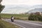 Biker in black leather outfit driving modern powerful motorcycle along sunny road on summer day.