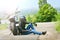 Biker in outfit sits next to his motorcycle on the road.