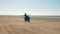 Biker riding motorcycle hands free on sandy beach through desert.