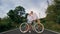 Biking road trip. Love couple on blue bike in white clothes on forest road. Just married woman and man kiss, hugs, stand