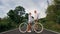 Biking road trip. Love couple on blue bike in white clothes on forest road. Just married woman and man kiss, hugs, stand