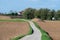 Biking trail through agriculture fields with brown soil, green crops and blue sky, Zellik, Belgium