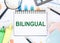 BILINGUAL text on white paper with office tools on office background