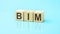 BIM - acronym from wooden blocks with letters, abbreviation BIM Building Information Modeling concept, blue background