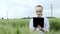 Biologist wearing white bathrobe is checking harvest progress on a tablet at the green wheat field. New crop of wheat is growing