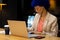 Biracial casual businesswoman with blue afro using laptop and writing in notebook at desk in office