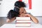 Biracial elementary schoolgirl leaning on stacked books at desk in classroom