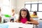 Biracial elementary schoolgirl reading book while sitting at desk in classroom