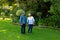 Biracial happy senior woman holding husband\\\'s hand while standing against plants and trees in park
