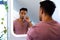 Biracial man looking at himself in mirror and brushing teeth in bathroom