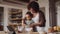 Biracial mother baking with her young daughter in a modern-styled kitchen, cracking eggs in bowl to whisk.