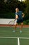 Biracial senior man hitting tennis ball with racket while playing tennis against trees at court