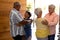 Biracial seniors embracing cheerful friends standing at doorway in nursing home