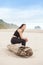 Biracial teen girl sitting on log quietly looking at ocean