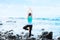 Biracial teen standing on rock by ocean doing yoga