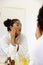 Biracial woman in bathrobe looking in mirror in sunny bathroom