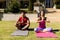 Biracial young couple practicing meditation in prayer pose while sitting on mats in yard