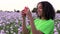 Biracial young woman walking through field of pink poppy flowers taking photographs on her smart phone