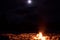 Birch log fire on winter snow on a dark full moon night