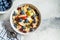 Bircher muesli or overnight oatmeal with apple, banana and blueberries in gray bowl, top view