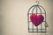 A bird cage with a red heart inside