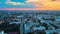 Bird's-eye view of city at blue dusk. Bright orange sunset sky over low houses.