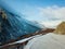 A bird\\\'s eye view of a ridgeline half-covered with snow in a forest with a sunburst in the upper left corner of the frame.