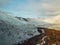 A bird\\\'s eye view of a ridgeline half-covered with snow in a forest with a sunburst in the upper left corner of the frame.