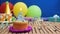 Birthday 6 cake with candles on rustic wooden table with background of colorful balloons, gifts, plastic cups and candies