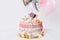 Birthday cake with decorated with candies, lollipop, marshmallows. Pink pastel color. Balloons on background