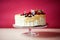 A birthday cake on a glass stand on the table, fruit on top.