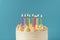 Birthday cake with white cream cheese frosting decorated with multicolored lit candles on a blue background. Happy Birthday