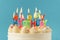 Birthday cake with white cream cheese frosting decorated with multicolored lit happy birthday text shaped candles on a blue